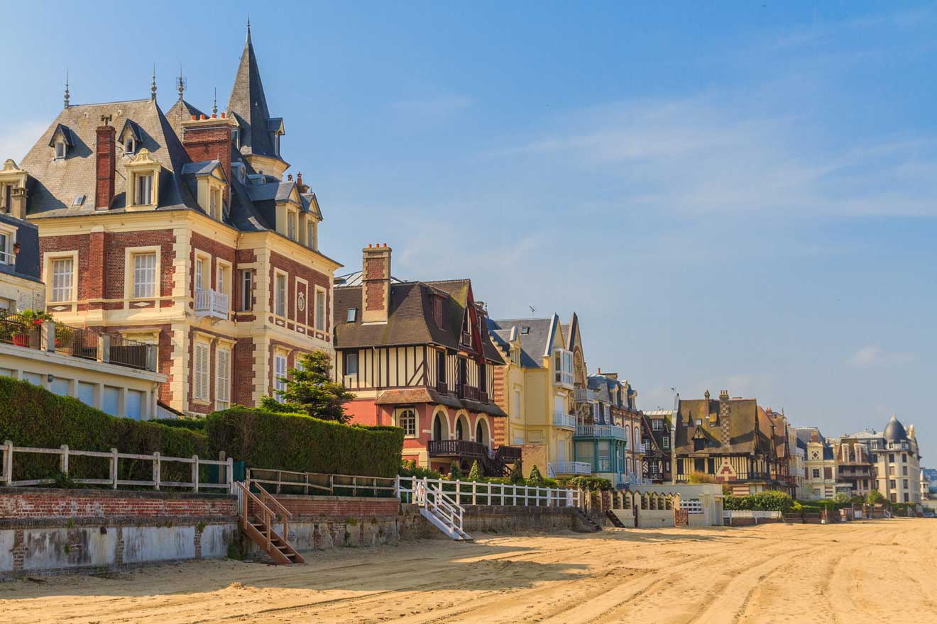 Row of elegant, multi-story houses with diverse architectural styles facing a sandy beach under a clear blue sky.