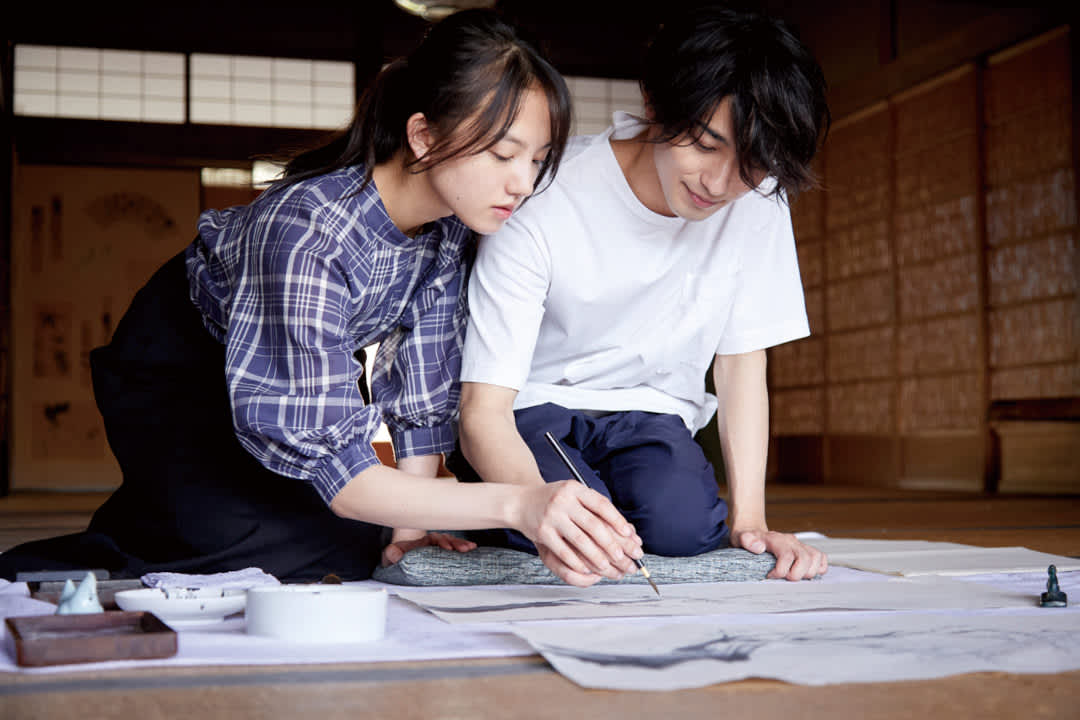 Promotional image for the film The Lines that define Me, with the two protagonists kneeling down and painting in the traditional art form of sumi-e